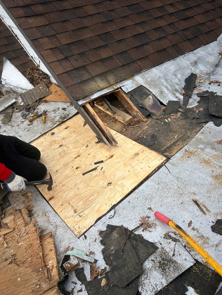 Roof repair work showing brown shingles, exposed wooden plywood decking, damaged underlayment, and repair tools on a construction site
