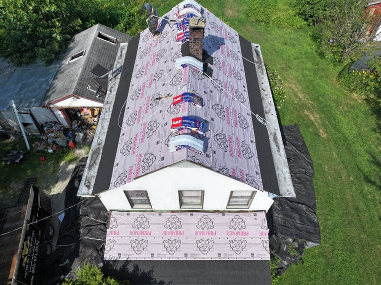 Aerial view of a residential roof covered with pink protective tarp and undergoing repair or renovation work