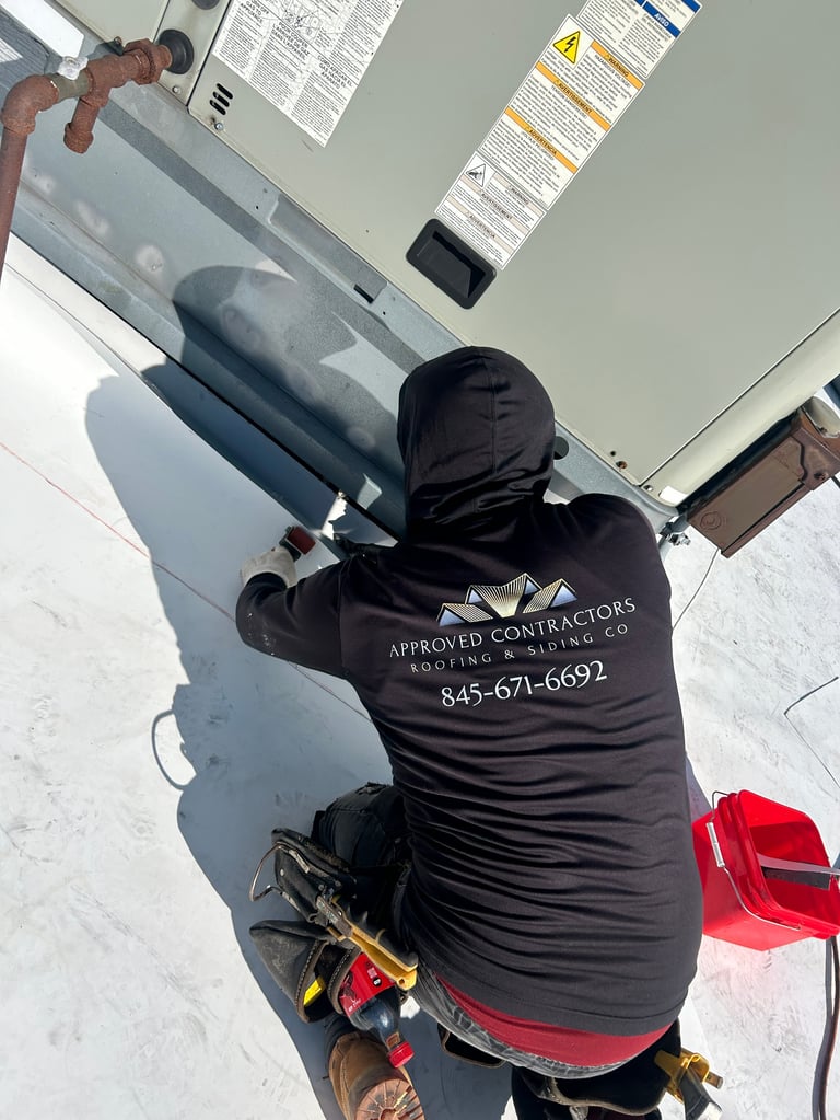 Worker in black jacket installing or repairing white HVAC ductwork on ceiling with tools nearby