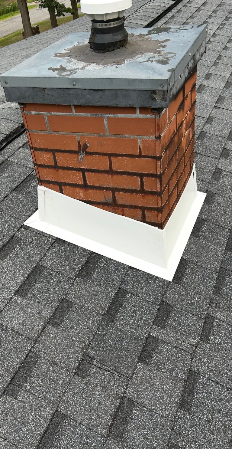 Brick chimney on asphalt shingled roof with metal cap and white base flashing