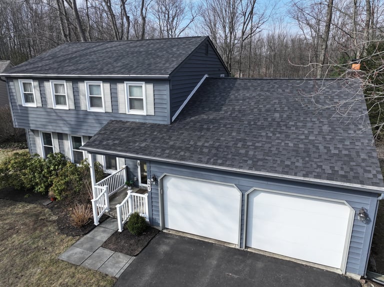 Two-story gray house with white garage doors, white trim windows, and dark gray roof surrounded by bare trees