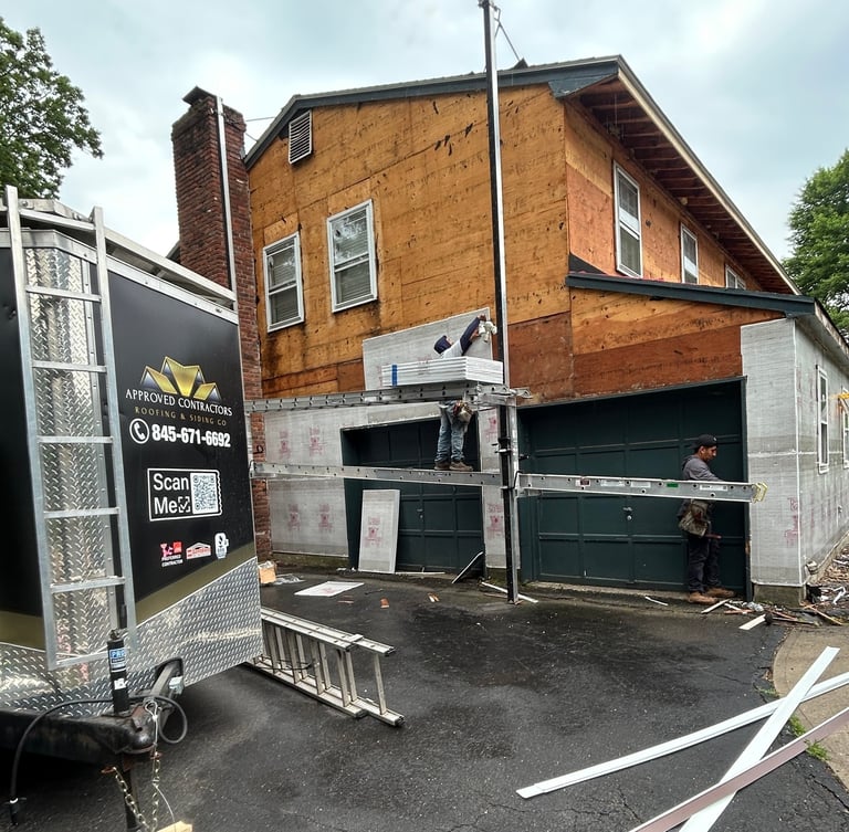 Damaged brick residential building with boarded-up garage doors and construction equipment nearby