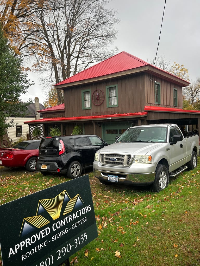 Red-roofed commercial building with brown siding, parked vehicles, and Approved Contractors roofing sign