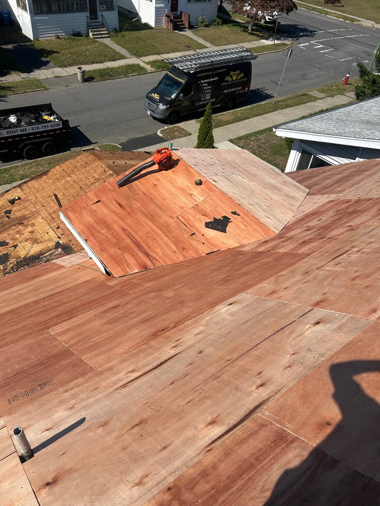 Aerial view of a residential roof under construction with wooden sheathing, an orange nail gun, and roofing contractor truck visible below