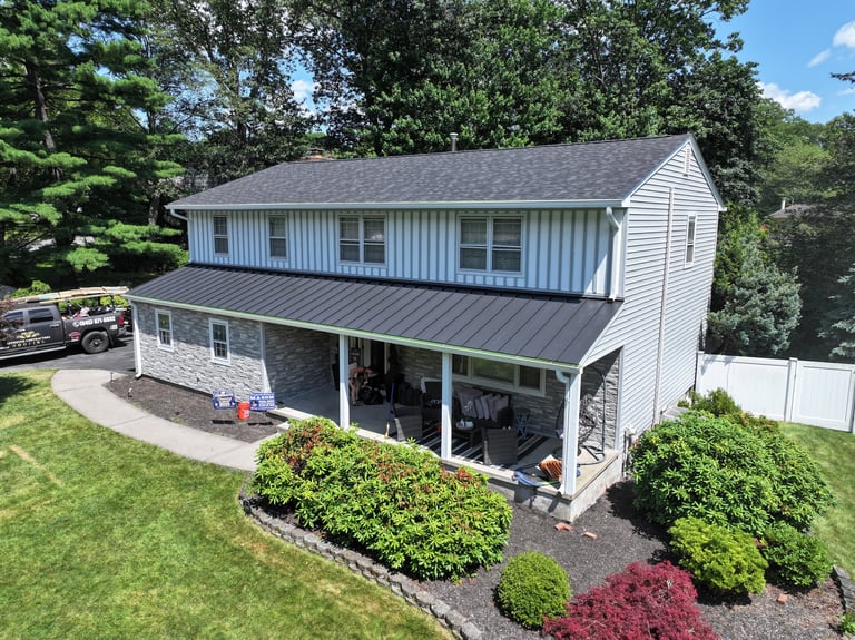 Aerial view of a two-story modern home with metal roof, white siding, front porch, and manicured landscaping with shrubs and trees