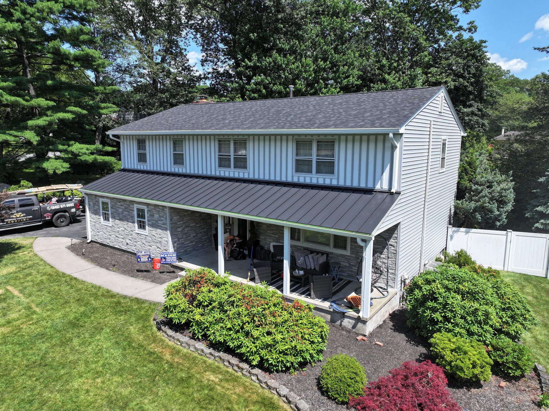 Two-story house with white siding and dark roof, front porch, landscaped yard with shrubs and mulch beds