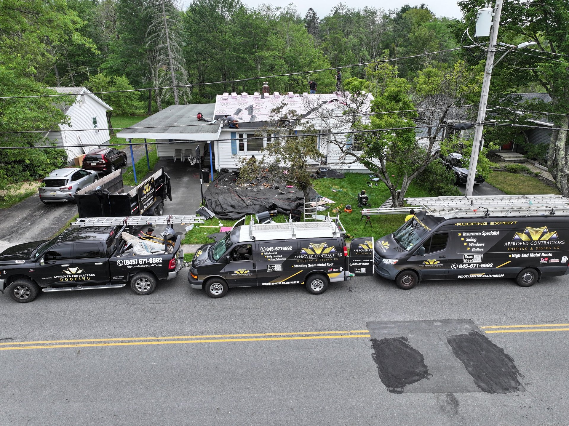 Three black excavation trucks parked in front of a house with debris and trees in background