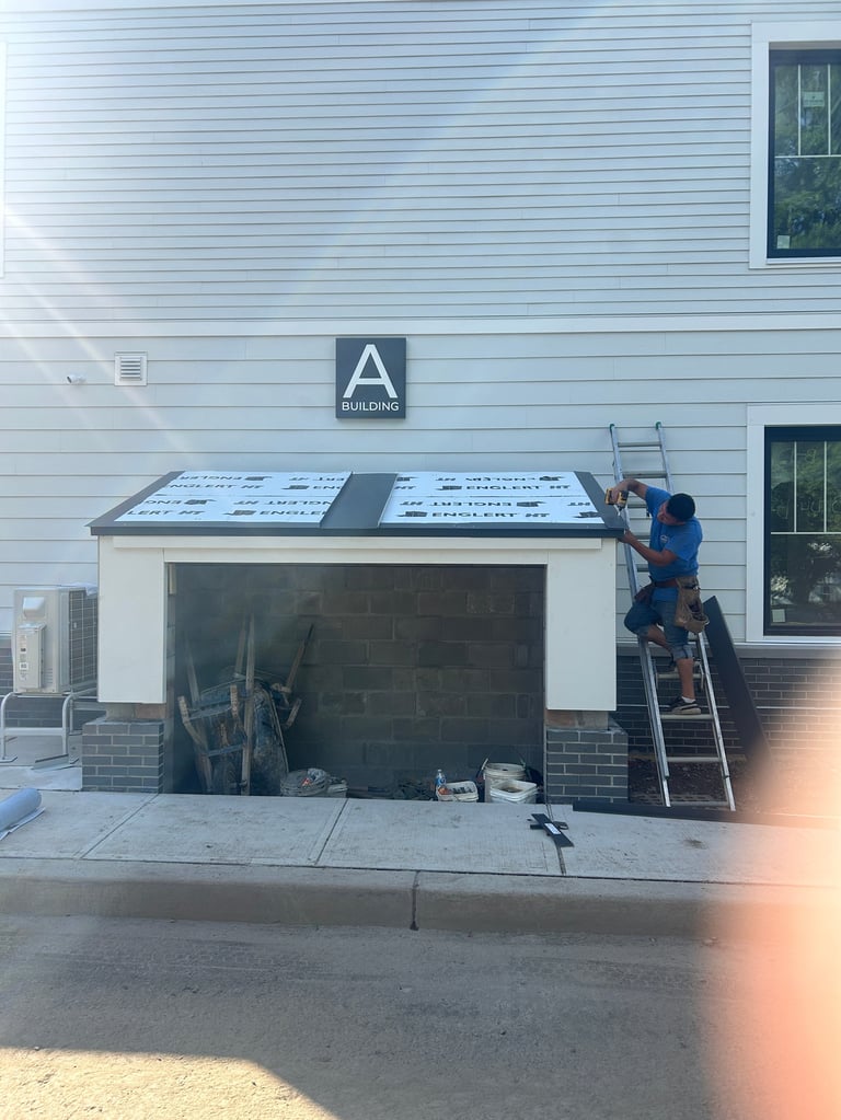 Worker on ladder installing roof panels above garage during construction on building with light blue siding