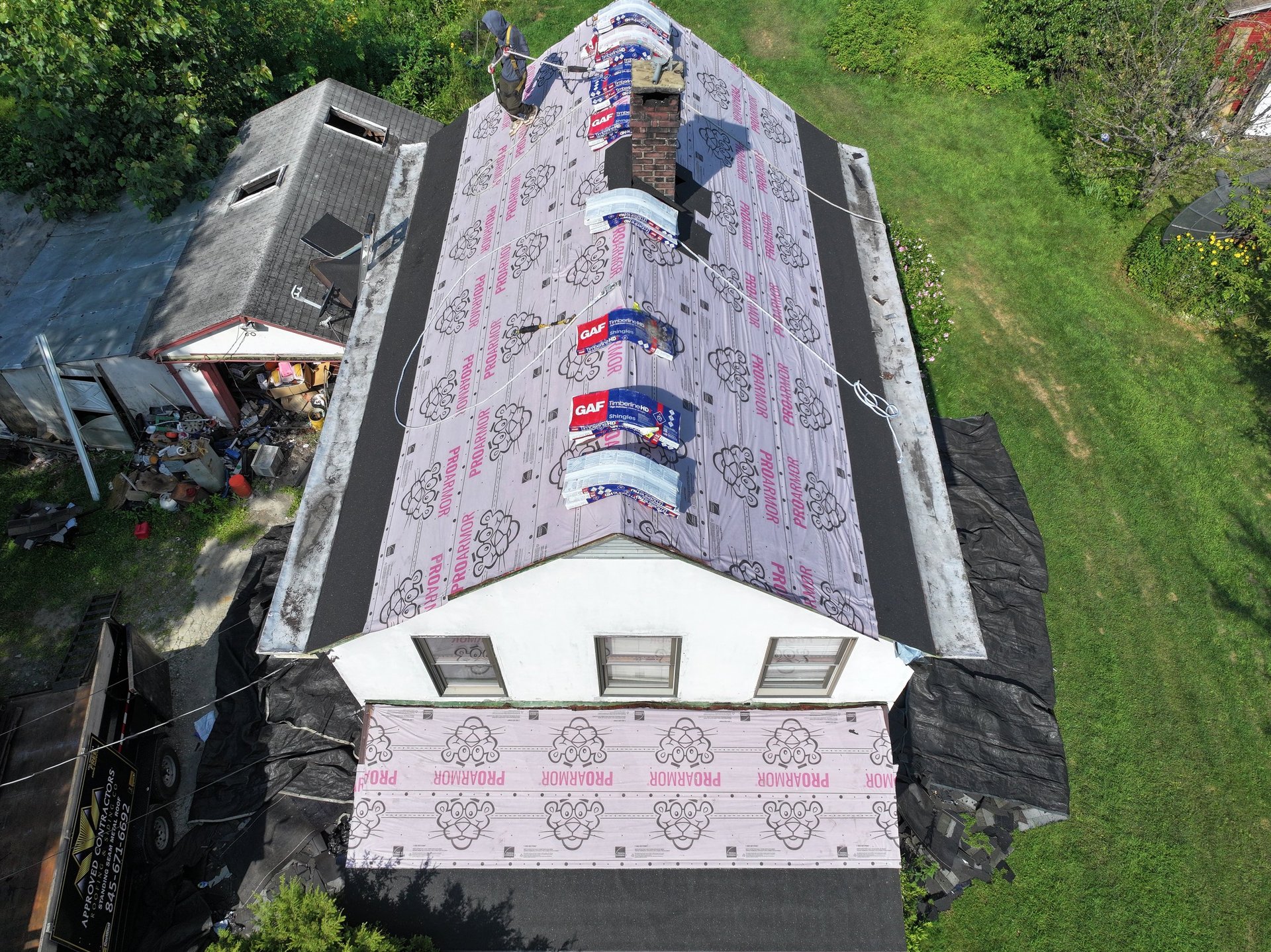 Aerial view of a house roof covered with pink protective tarps and construction materials during renovation work