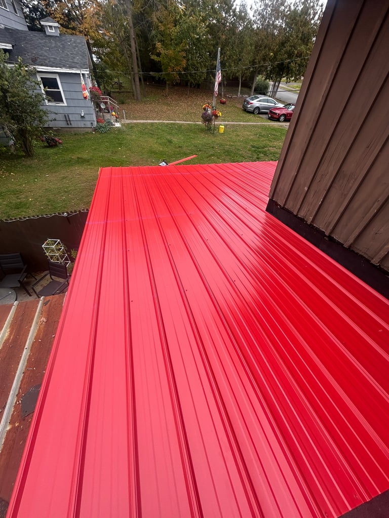 Red corrugated metal roof viewed from inside, overlooking a residential backyard with house, trees, and parked cars