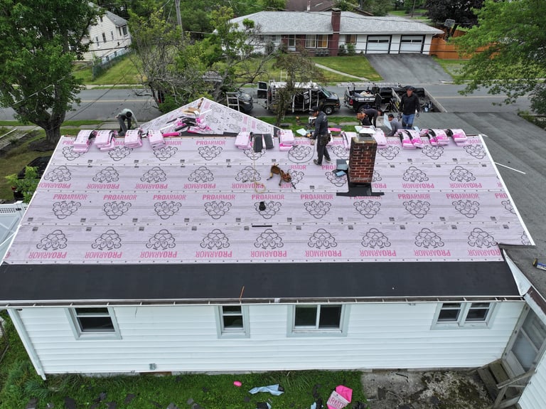 Aerial view of a house roof being replaced with pink underlayment and workers on top